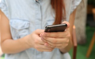 Woman in blue button down shirt holds her cell phone.