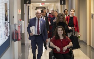 Congressman Paul Tonko tours the RNA Institute alongside members of UAlbany leadership. In this image, nine people are proceeding down a hall in the RNA Institute, among the labs. The group is led by Paul Tonko on the left and guest speaker Jennifer Rittner is being pushed in a wheelchair on the right. UAlbany President Havidán Rodríguez and RNA Institute Director Andy Berglund are in conversation behind them.