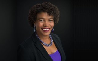 A smiling woman with curly brown hair, silver earings and a beaded necklace