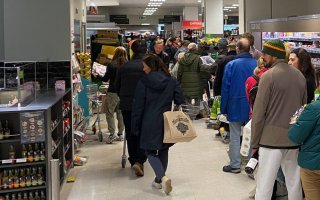 People stand in line holding their goods, waiting to check out of a grocery store.