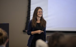 A woman speaks in front of a projector screen at the UAlbany mathematics conference.
