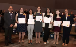 President Rodriguez stands beside six smiling young women holding awards certificates