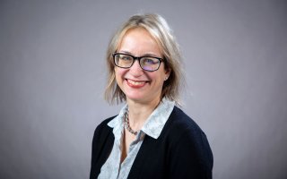 A woman with short blonde hair and glasses smiles for a portrait.