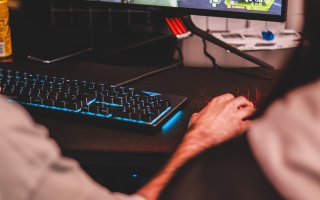 A hand hovers over a computer mouse next to a lit-up keyboard and computer screen.