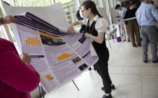 A woman in braids and glasses unrolls a research poster to place it on an display easle