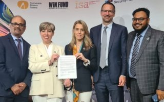 Five people standing in a line shoulder to shoulder, including two women holding a signed document.