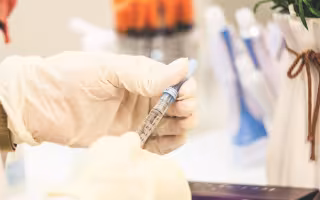 Hands wearing protective plastic gloves hold a syringe