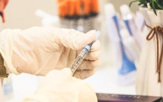 Hands wearing protective plastic gloves hold a syringe