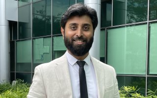 Arun Chandrasekaran wears a cream colored linen suit jacket and dark blue tie for a portrait outside the RNA Institute.