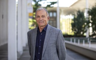 Chemist Igor Lednev stands on the Academic Podium in a grey suit.