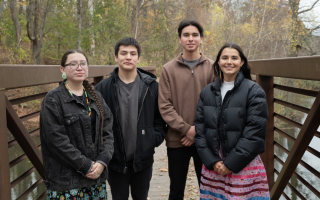 Two young men and two young women stand on a bridge over Parker Pond on the UAlbany campus on an overcast fall day.