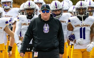 UAlbany head football coach Greg Gattuso leads his team onto the field.