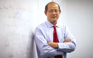 Professor of Mathematics Kehe Zhu stands next to an equation on a whiteboard.