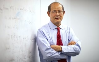 Professor of Mathematics Kehe Zhu stands next to an equation on a whiteboard.
