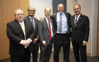 Five men wearing suits pose and smile for a casual group portrait.