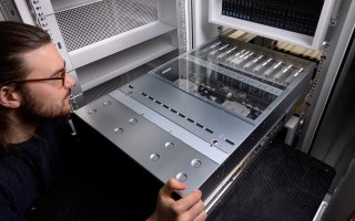 A person in the foreground slides a metallic silver computer node into a server rack.