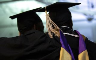 The backs of two graduates are seen in silhouette wearing mortorboards and graduation regalia