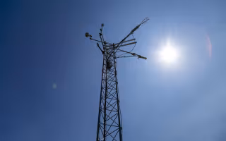 The sun shines behind the top of a New York Mesonet station weather tower.