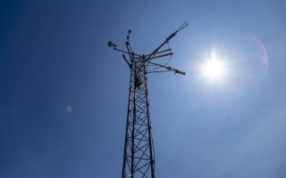 The sun shines behind the top of a New York Mesonet station weather tower.