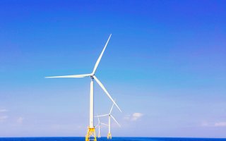 Three white wind turbines emerge from blue water against a blue sky.