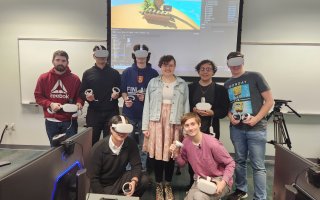 CEHC Instructor Claire Thomas stands in the middle of students wearing Meta Quest 2 headsets in front of a projector screen inside a computer lab at the Science Library.
