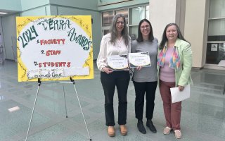 Three women pose for a portrait holding certificates next to a poster board that says "2024 Terra Awards"