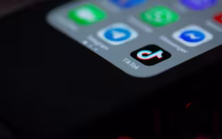 Image is mainly black, showing a corner of a glowing smartphone with several icons for apps including TikTok.