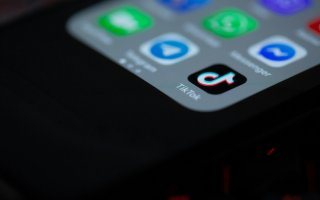 Image is mainly black, showing a corner of a glowing smartphone with several icons for apps including TikTok.