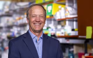 A smiling man in a blue blazer stands in a laboratory.