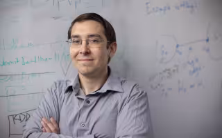 UAlbany Assistant Professor Abram Magner stands in front of his white board with equations in the background. (Photo by Brian Busher)