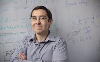 UAlbany Assistant Professor Abram Magner stands in front of his white board with equations in the background. (Photo by Brian Busher)