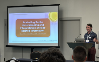 Bruce Pollock uses a projector screen and podium to present on heat warning communication. 