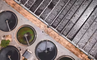 Aerial image of a wastewater treatment facility. The top right half of the image shows water being treated in a rectangular holding pool. On the bottom left, water is held in circular tanks.