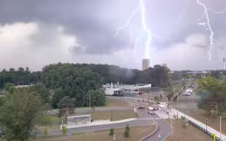A photo taken from an elevated position showing two flashes of lightning, one of which is striking a rectangular tower in the distance.