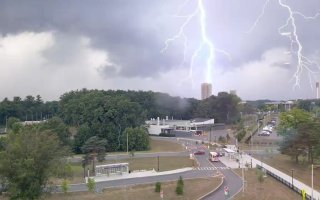 A photo taken from an elevated position showing two flashes of lightning, one of which is striking a rectangular tower in the distance.