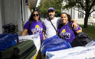 A new student wearing a purple UAlbany shirt stands with her family on move-in day.