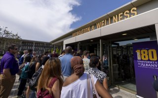 A group of people head into a building entrance with the words "Recreation & Wellness" in metal letters above the door. 