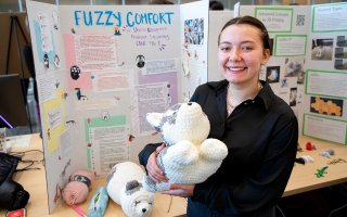 Student Daria Kolmogorova holds a stuffed animal in front of her poster project at CEHC's Fall 2023 Showcase.
