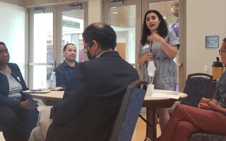 Woman stands at a table of five, sharing top takeaways from their group discussion. 