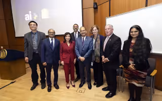 Group of seven individuals standing in front of University at Albany and AI logos, smiling in a conference room setting.