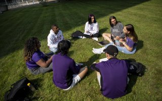 Students seated in a circle on the grass outside building 