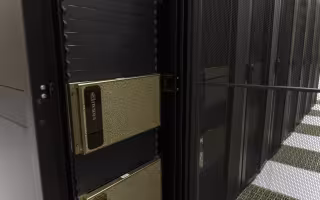 A close-up of a silver rectangular GPU system installed in a row of tall, black server racks. 