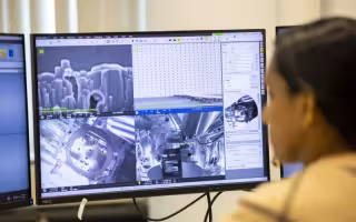 A woman's face is blurred in the foreground as she looks at computer screens with gray images that show heavily magnified computer chip designs. 