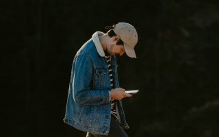 A young man walks outside in nature with his head down staring at an iPhone