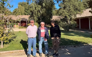 Three older men stand outside on a bright sunny day wearing sunglasses in a courtyard of Chilean fruit drink company.
