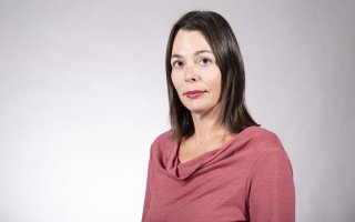 A woman with shoulder-length brown hair in a pink top poses for a portrait against a gray backdrop.