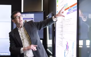Nick Bassill points at a weather briefing on a projection screen inside UAlbany’s xCITE laboratory.