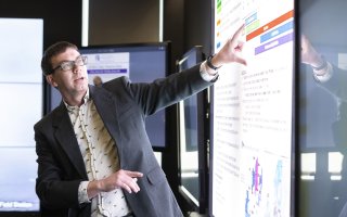 Nick Bassill points at a weather briefing on a projection screen inside UAlbany’s xCITE laboratory.