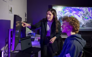 Allison Finch points at a computer screen inside UAlbany's State Weather Risk Communication Center.