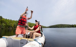 Paleoclimate researcher Aubrey Hillman and graduate student Sumar Hart hold up a sediment core from a research boat on Black Pond.